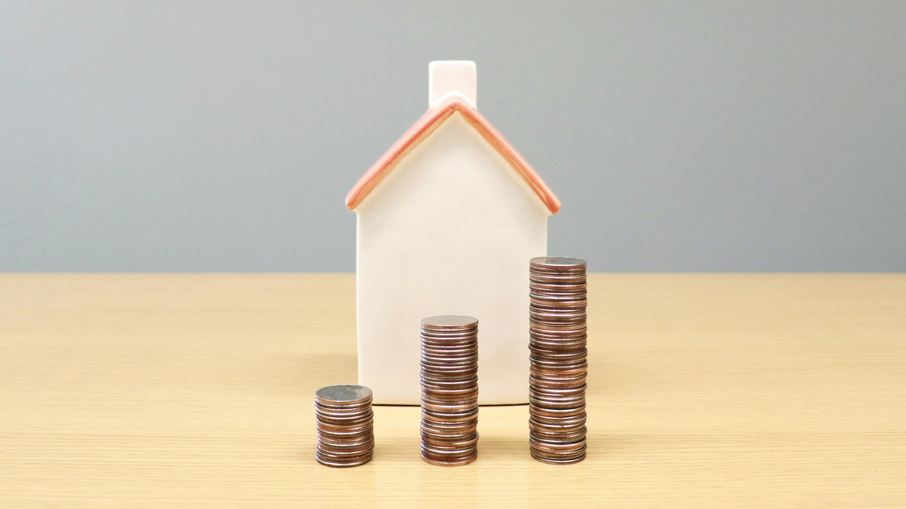 小さな家の模型と、積み上げた硬貨